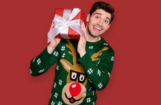 Mann in Weihnachtspullover hält Weihnachtsgeschenk und lächelt